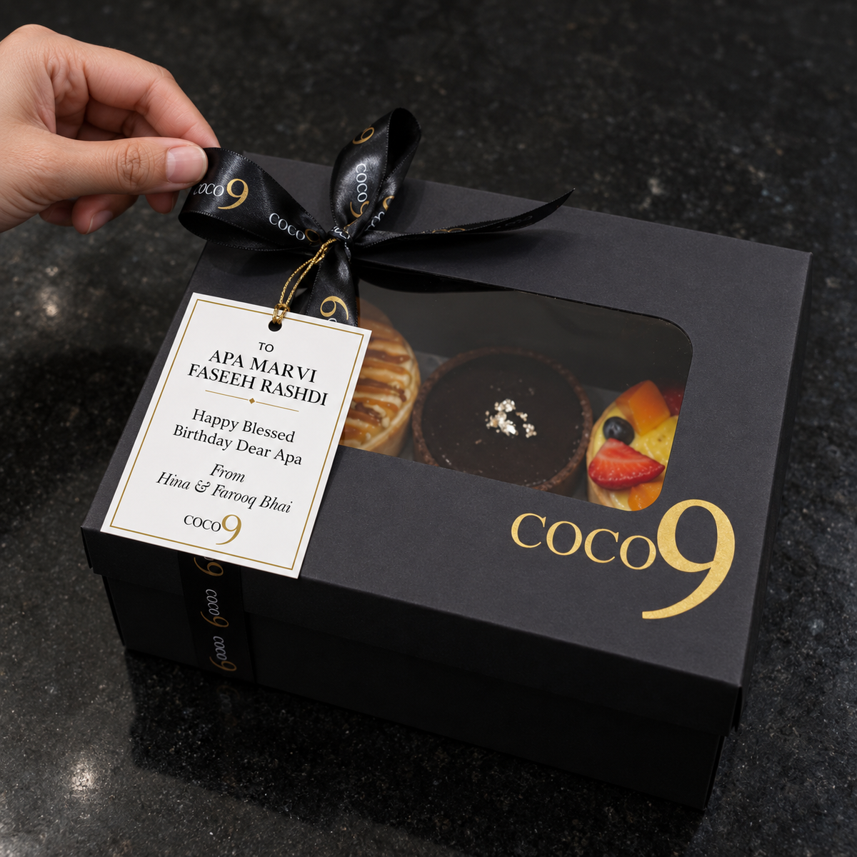 Hands finishing a box in the kitchen — tying ribbon or placing the card.