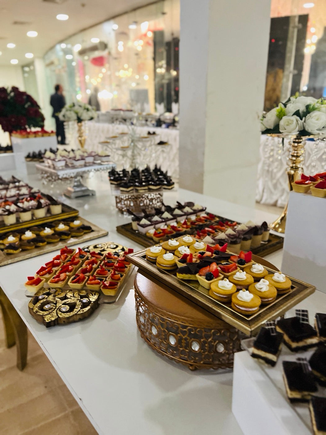 Coco 9 bite-size tarts and shooters on gold risers, with white flowers behind