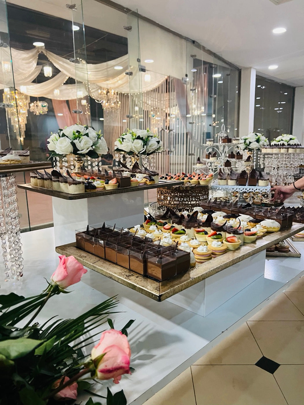 A Coco 9 dessert table of shooters and tarts on glass and gold stands, with white roses
